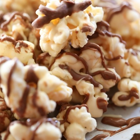 Avalanche Popcorn onto of parchment paper with chocolate drizzle.