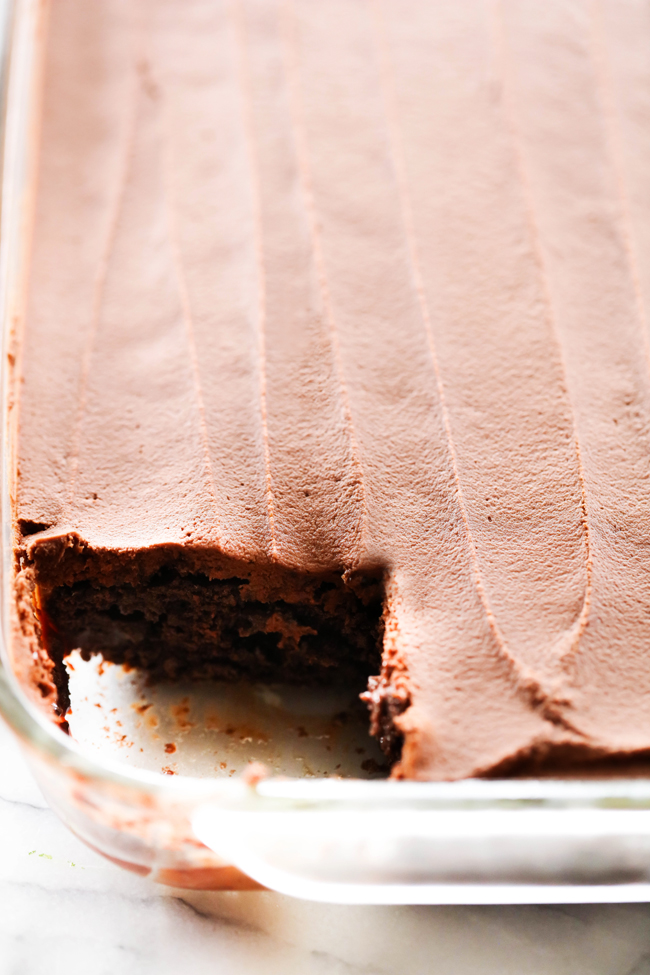 Rich Dense Chocolate Poke Cake in a clear baking dish with corner piece removed.