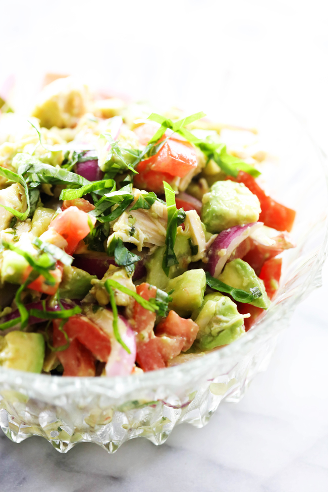 Chicken Avocado Chopped Salad in clear salad bowl and garnished with fresh chopped basil.
