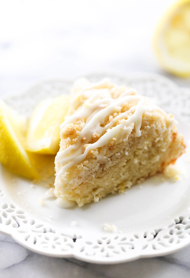 Slice of Lemon Crumb Cake on white plate next to slices of lemon.