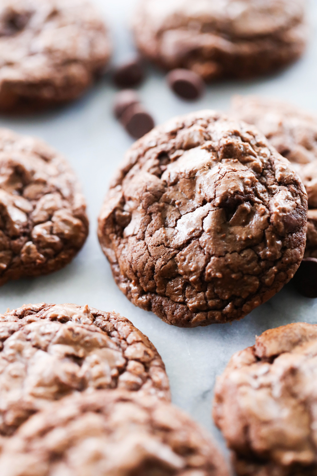 Soft and Chewy Double Chocolate Cookies on marble slab with chocolate chips scattered around.