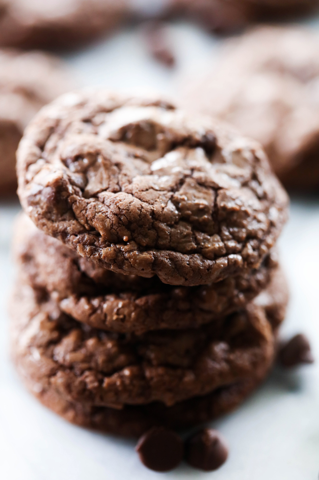 Soft and Chewy Double Chocolate Cookies stacked on top of each other on a marble slab with chocolate chips scattered close by.