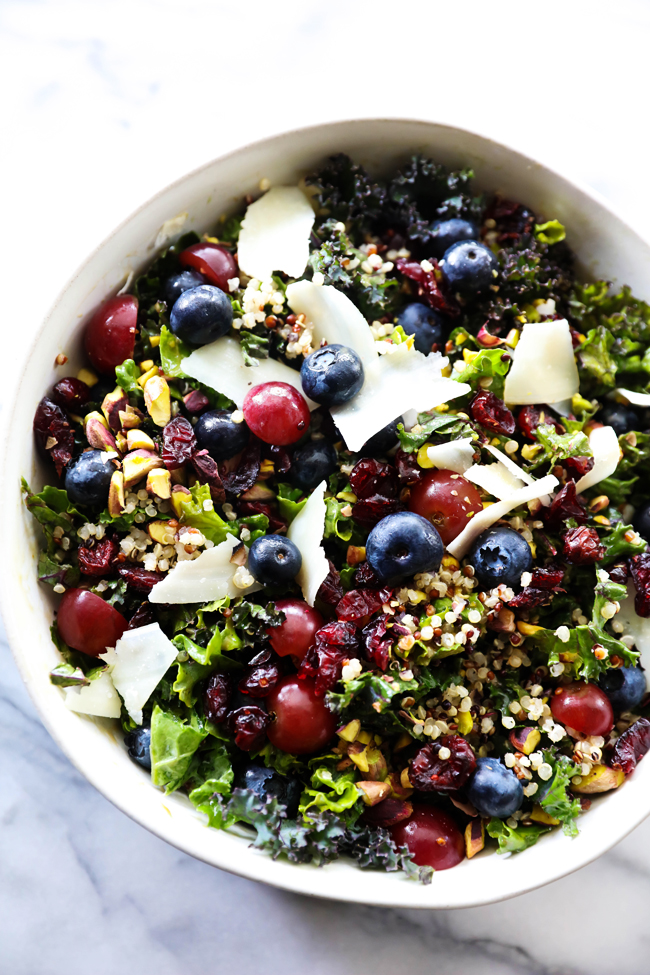 Overhead view of Kale and Quinoa Salad with blueberries, grapes, raisins, flakes of cheese, quinoa and kale.