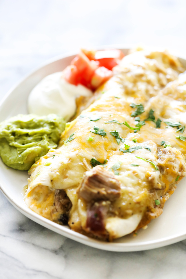 Two Chile Verde Pork Enchiladas on a white plate and garnished with guacamole, sour cream and fresh chopped tomatoes.
