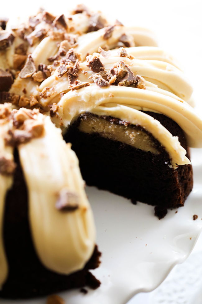 Chocolate Peanut Butter Cheesecake Bundt Cake with slice removed to reveal center on a white cake stand.