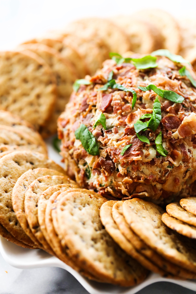 Spinach Artichoke Cheese Ball garnished with fresh chopped spinach surrounded by crackers on white serving tray.