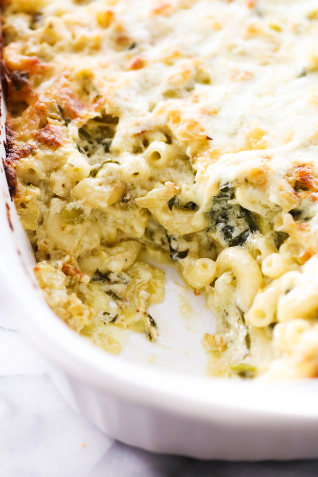 Spinach Artichoke Mac and Cheese in a white casserole dish with corner scoop removed.