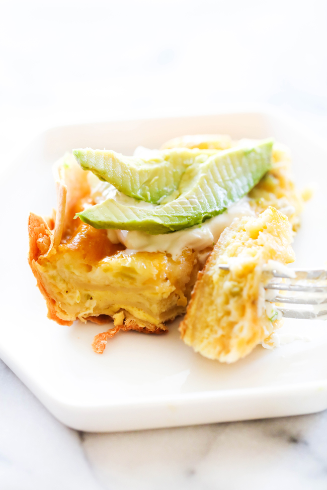 Slice of Chile Relleno Casserole on a white plate with fork garnished with sliced avocado and sour cream.