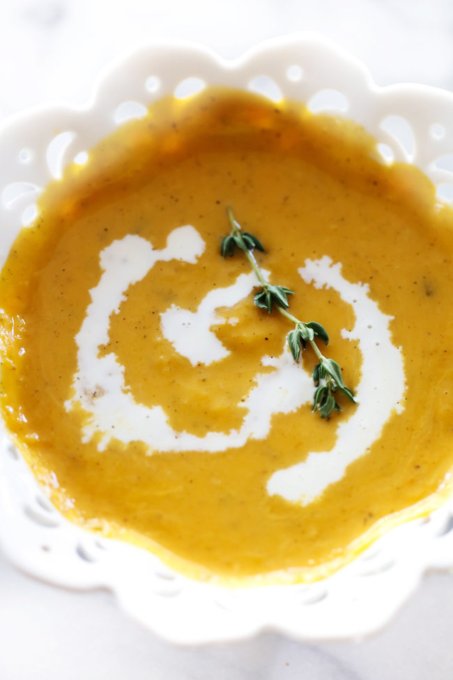 Overhead view of Butternut Squash Soup in a white bowl garnished with heavy cream and rosemary.