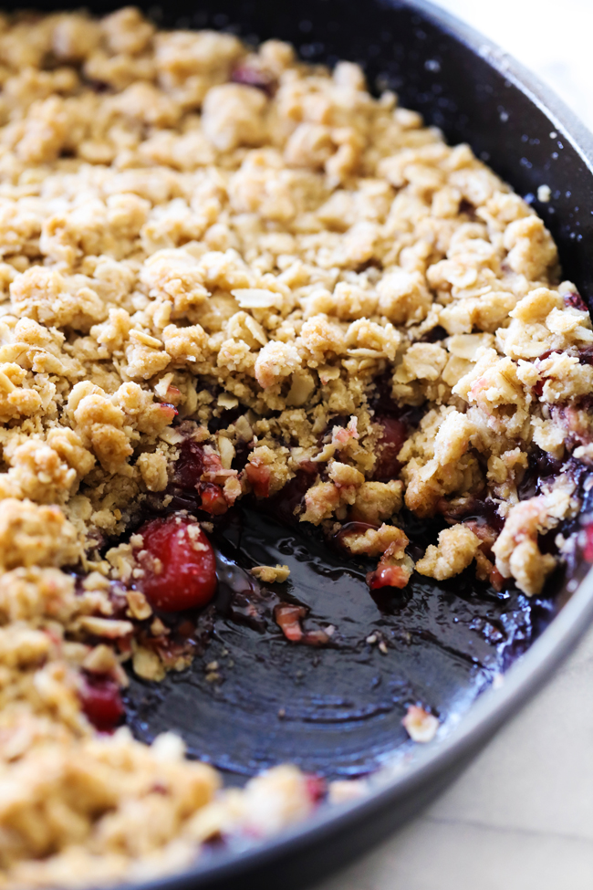 Cherry Crisp served in a cast iron skillet with a scoop removed.