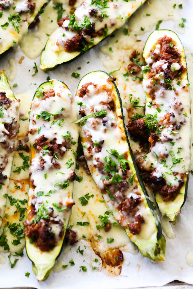 Zucchini sliced in halves stuffed with a blend of sausage, herbs, spices and cheese. Displayed on baking sheet and garnished with parsley.